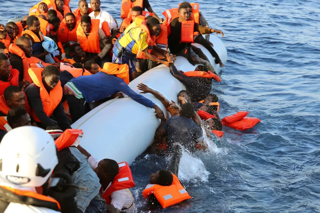 migranti africani su un gommone aiutano altri uomini a restare a galla